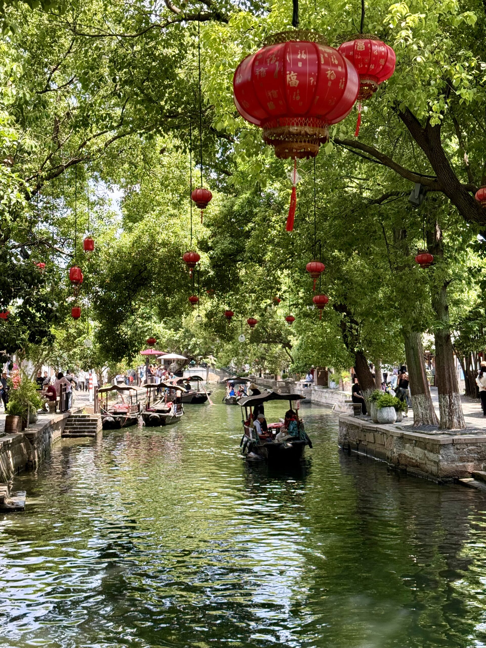 Canal boats beneath red lanterns and leafy trees in Zhujiajiao Water Town